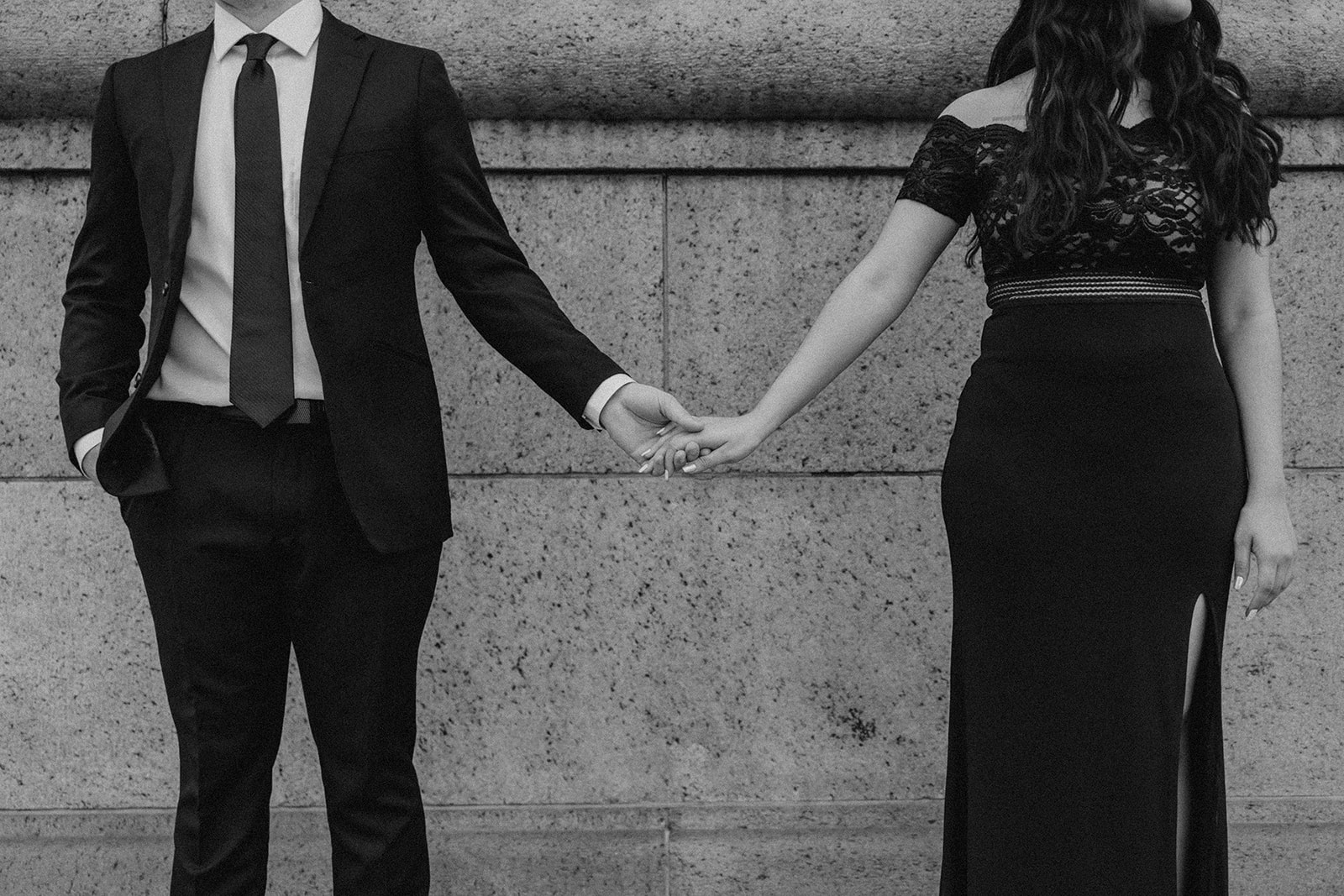 couple hold hands in front of a stone wall 