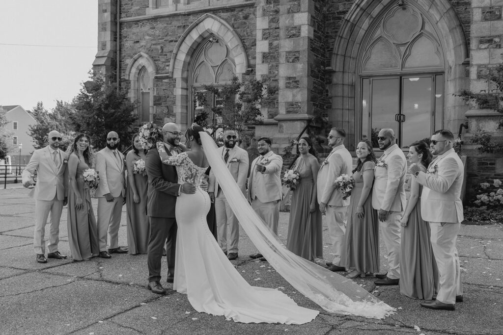 bride and groom pose together in front of their wedding party outside their classy church wedding venue