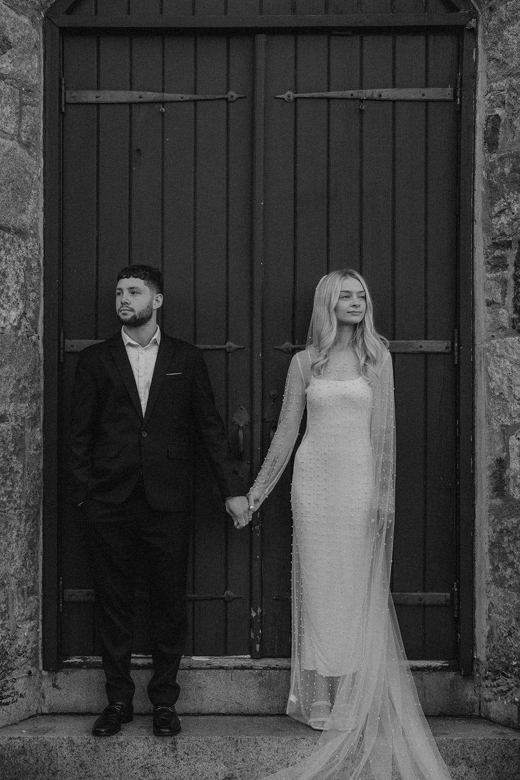 bride and groom hold hands posing in front of a black door 