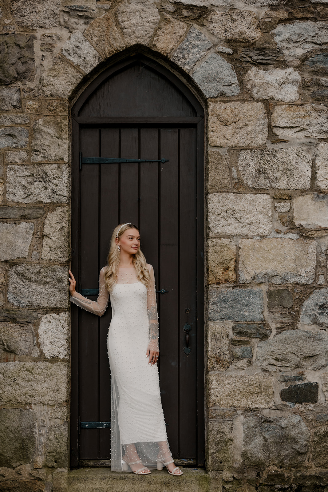 stunning bride is looking to the side while leaning against stone wall