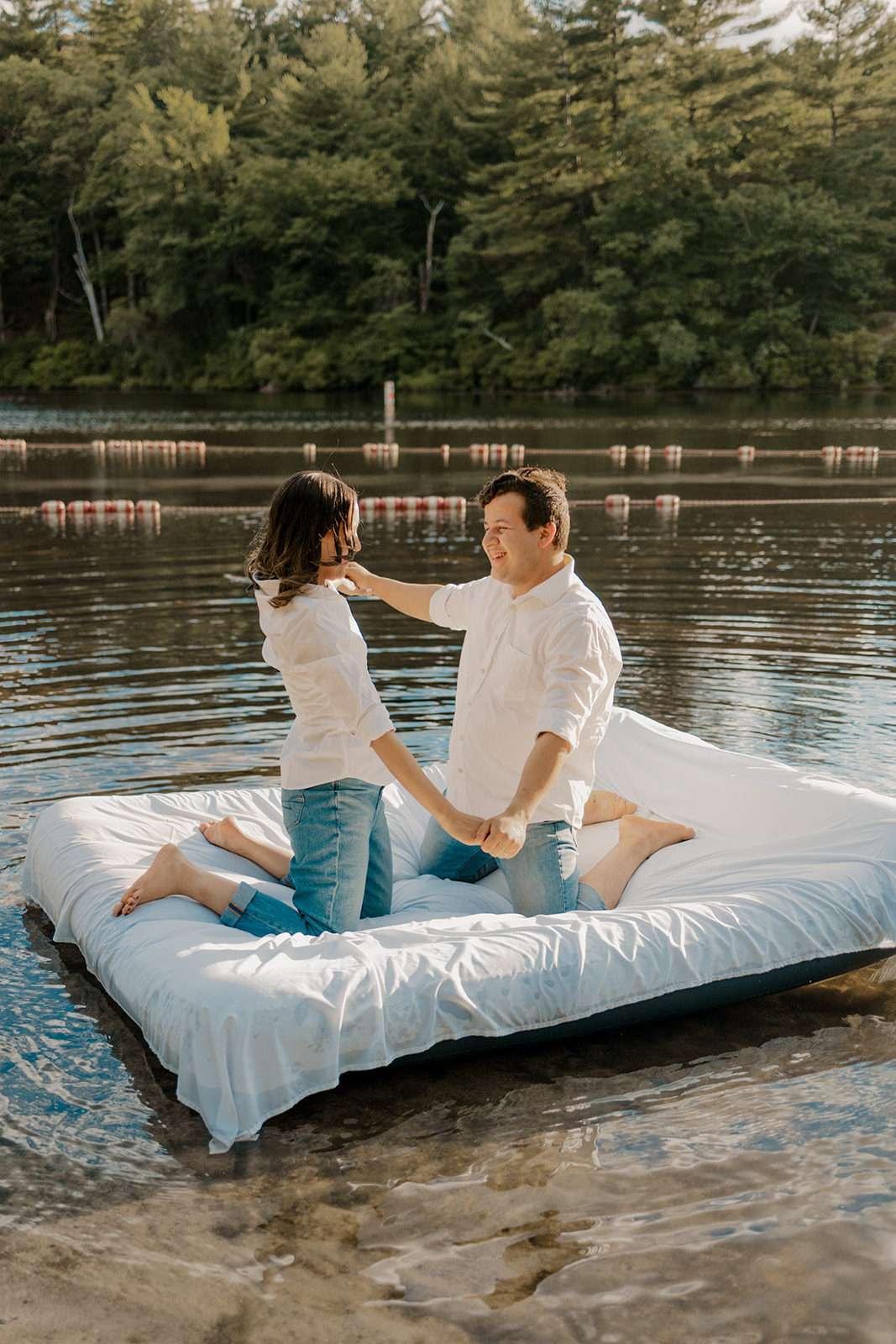 stunning couple pose on an air mattress floating on a lake during their fun New England engagement photoshoot