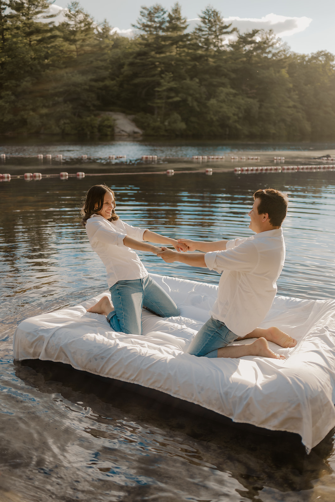 stunning couple pose on an air mattress floating on a lake during their fun New England engagement photoshoot