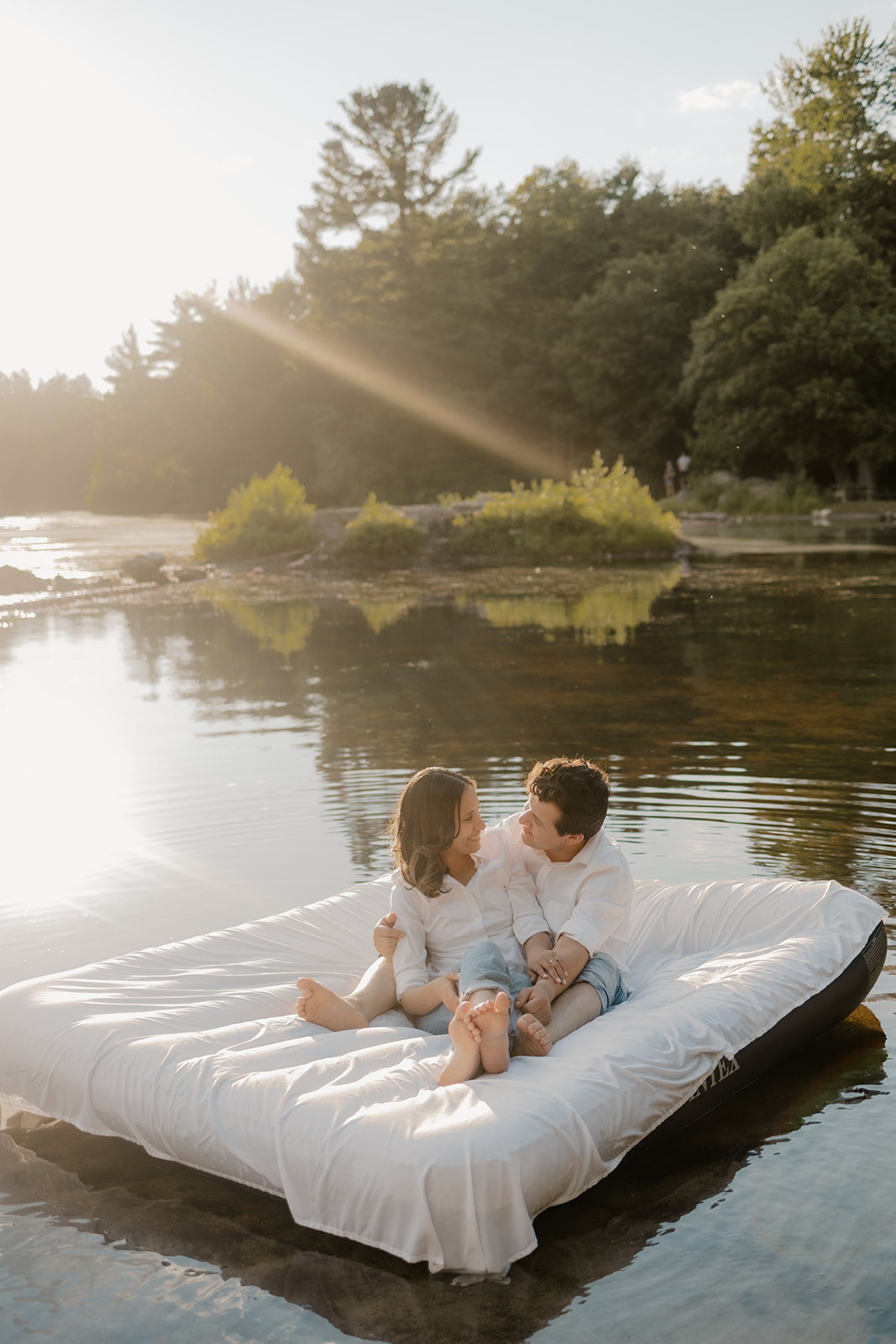 stunning couple pose on an air mattress floating on a lake during their fun New England engagement photoshoot