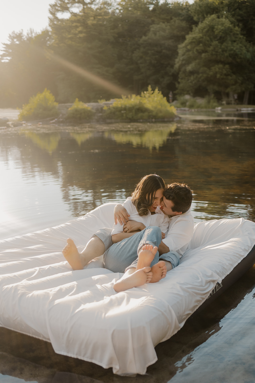 stunning couple pose on an air mattress floating on a lake during their fun New England engagement photoshoot