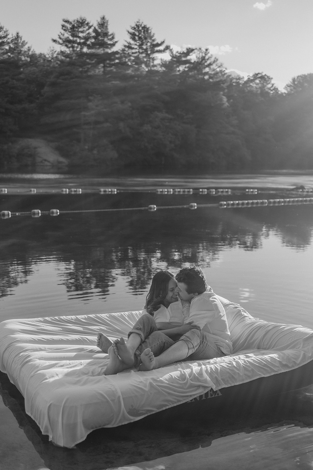 stunning couple pose on an air mattress floating on a lake during their fun New England engagement photoshoot