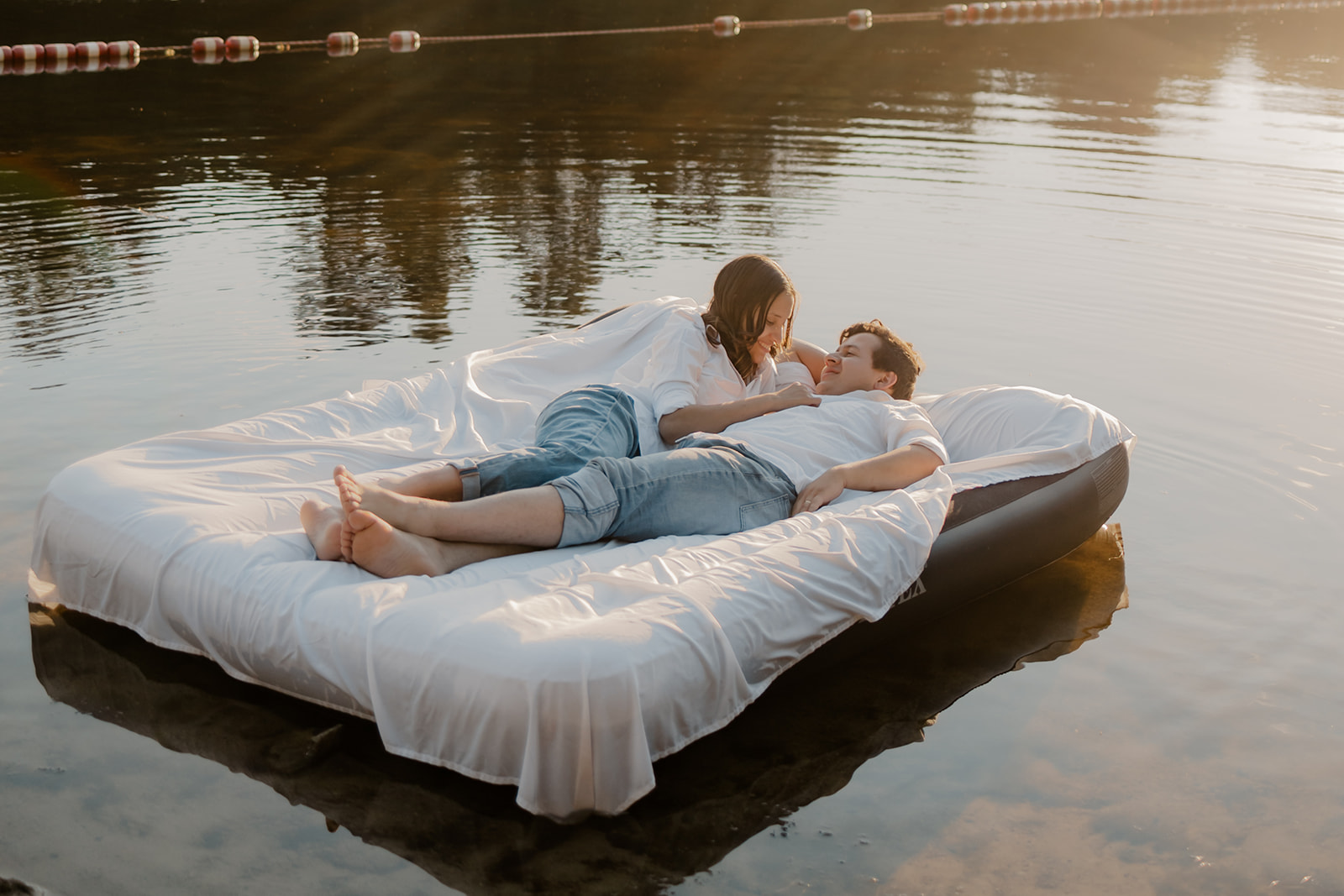 stunning couple pose on an air mattress floating on a lake during their fun New England engagement photoshoot