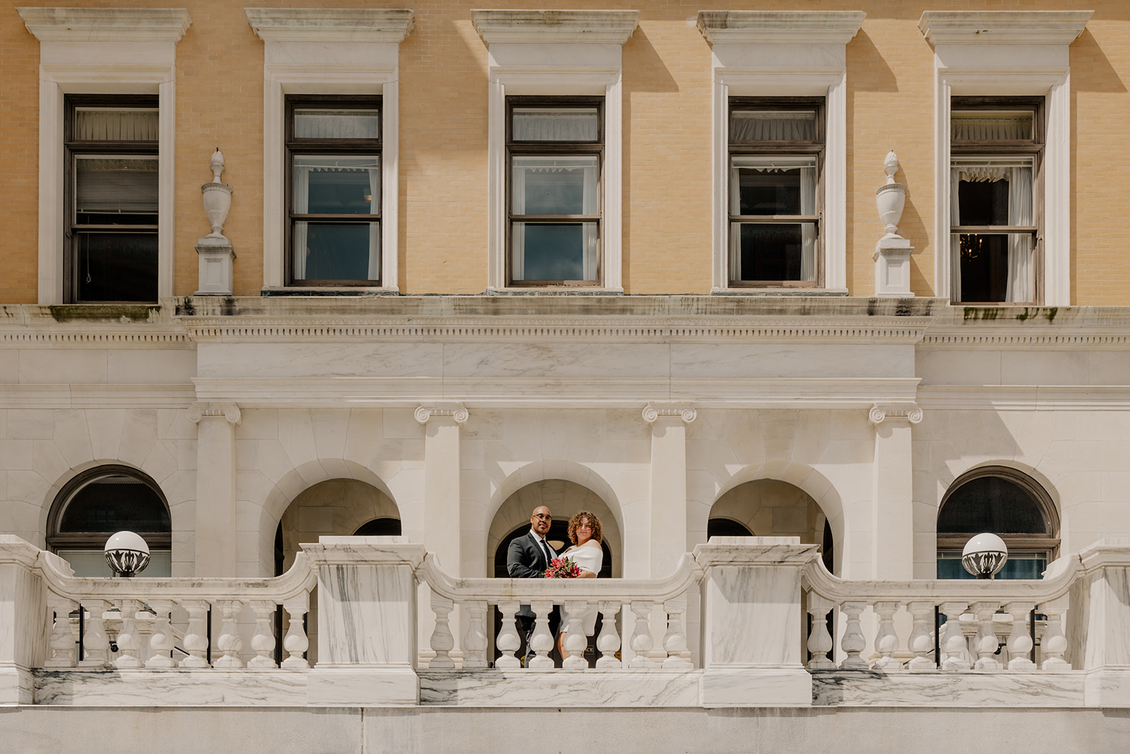 stunning bride and groom pose together on the state house balcony